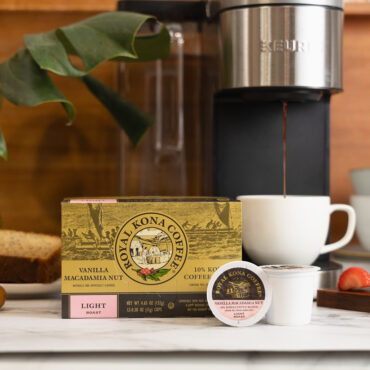 Royal Kona single serve coffee pods, 10% Kona Vanilla Macadamia, next to coffee machine