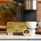 Royal Kona single serve coffee pods, 10% Kona Vanilla Macadamia, next to coffee machine