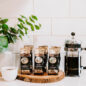 Six bags on coffee counter with a French Press next to them.